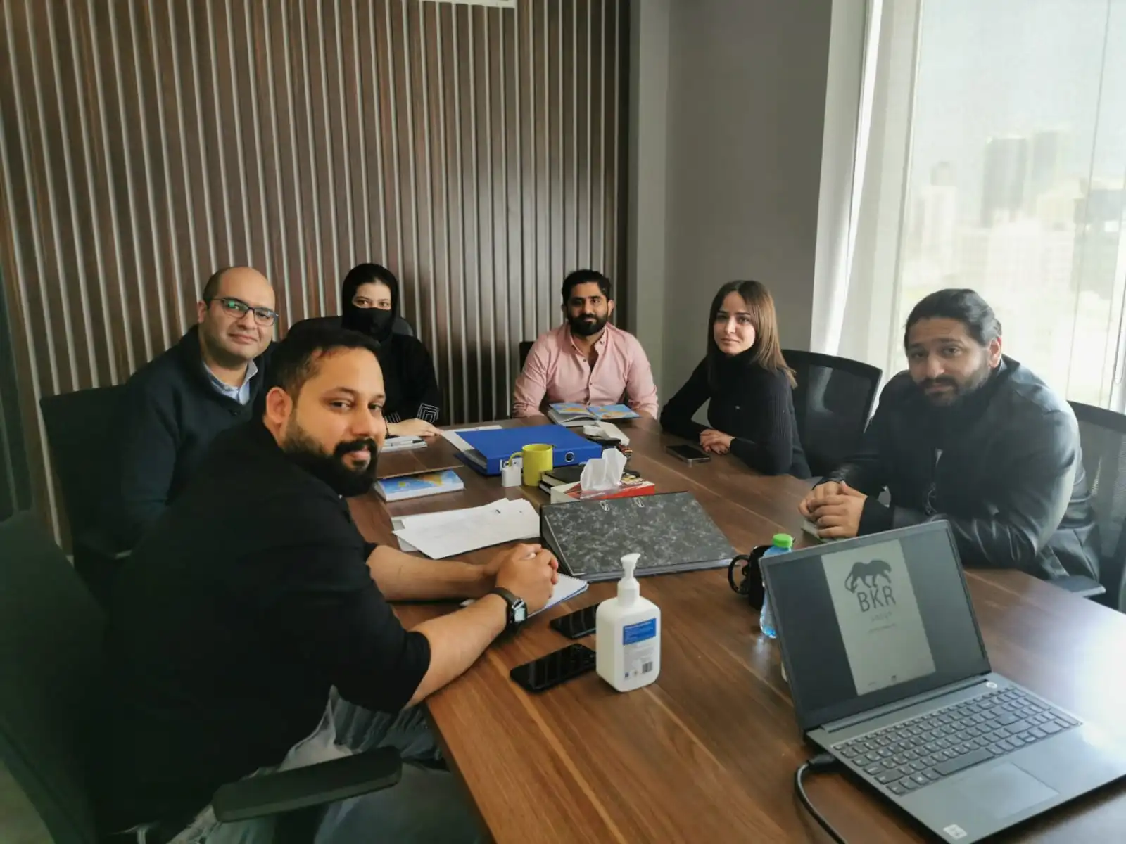 BKR Group staff members sitting around a wooden table in an office looking towards the camera.