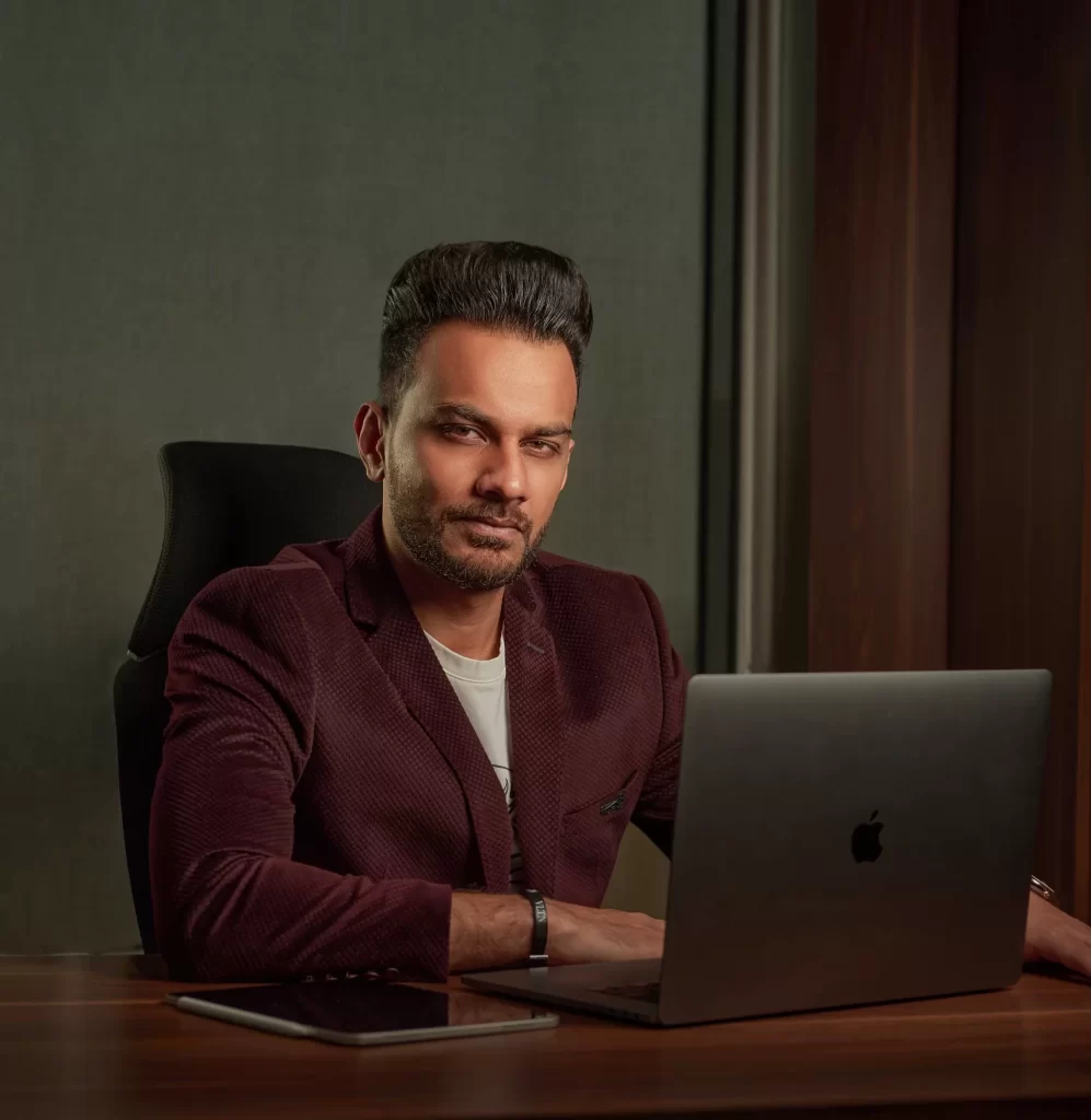 Bilal Khalid Rana, BKR Group's founder and CEO, sitting behind a desk and computer in a professional red suit.