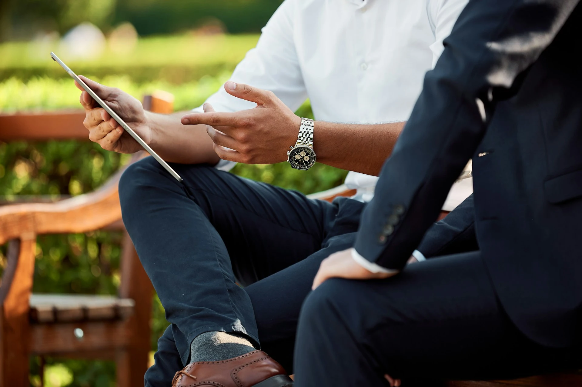 Businessman gestures towards an iPad, seemingly explaining something to another businessman.