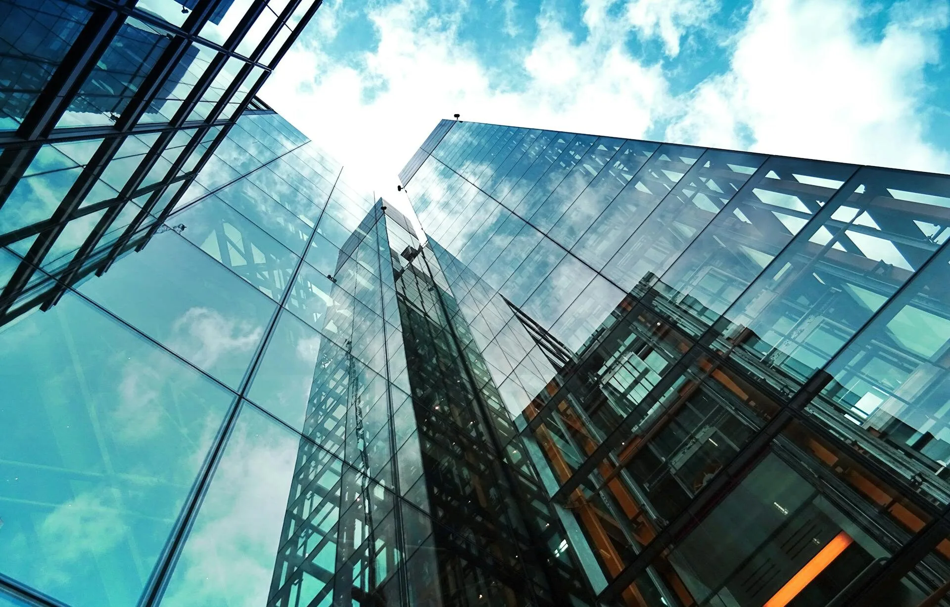 Glass skyscraper reflecting the clouds and sun on a bright day.