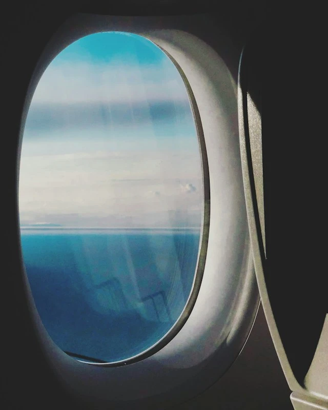 View out of an oval airplane window of the horizon across the sea.